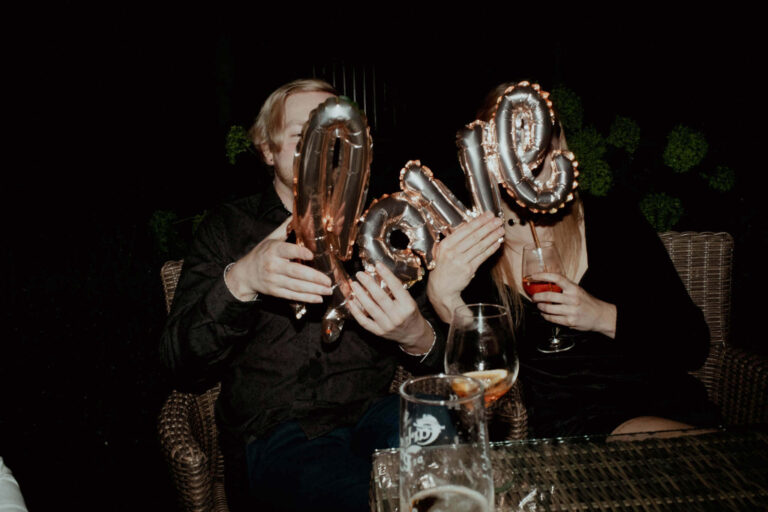 Chłopak i dziewczyna chowają się za balonem napis love