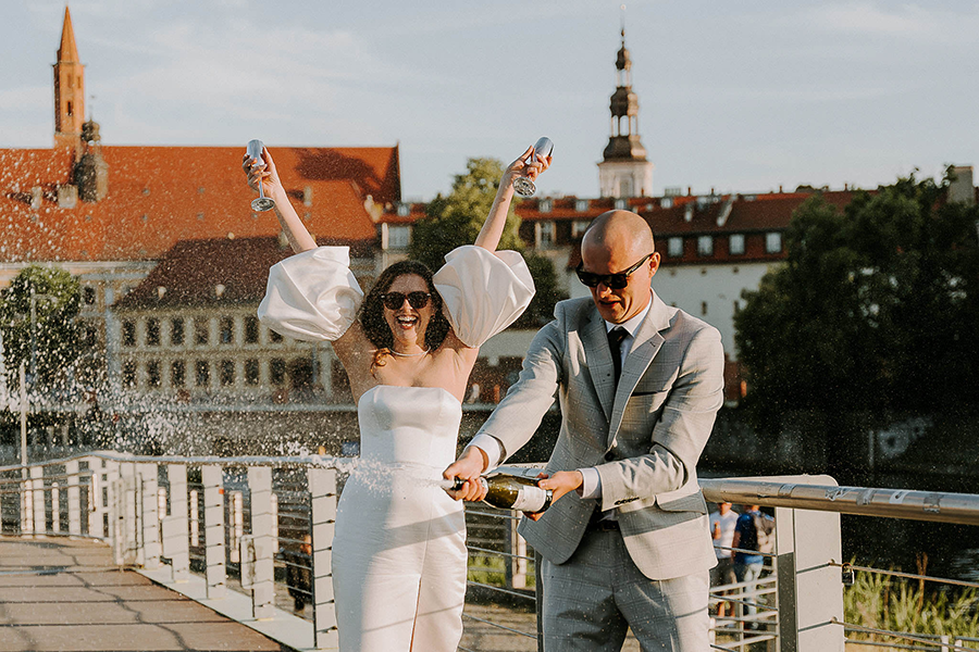 para młoda otwiera szampana na tle ostrowa tumskiego